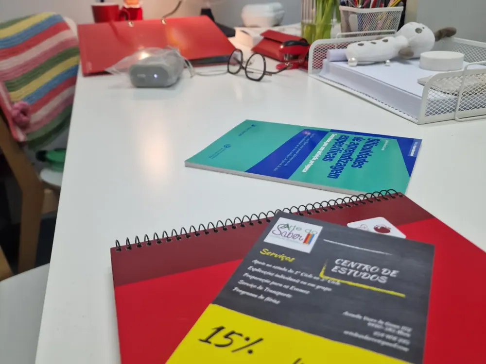 Mesa de trabalho com cadernos, material escolar e um flyer do centro