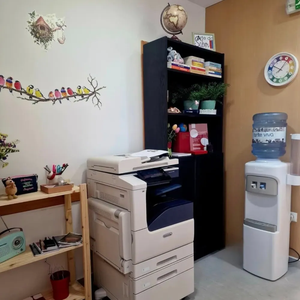 Zona de receção do centro, com fotocopiadora, dispensador de água e decoração de passarinhos na parede